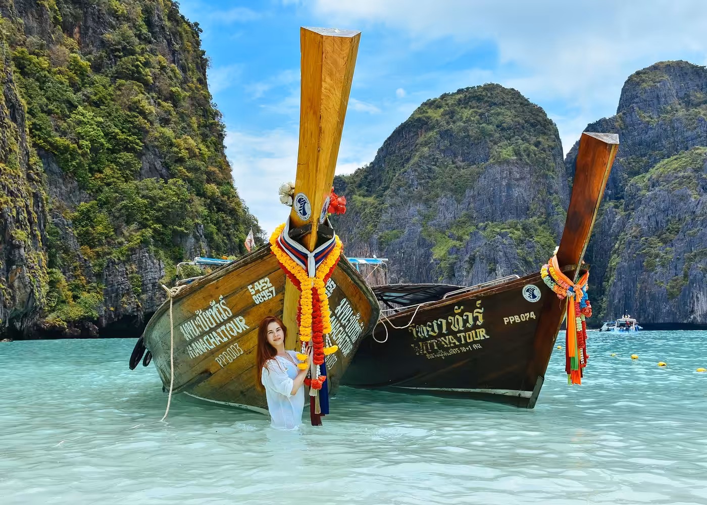 Tourist posing with traditional Thai longtail boats decorated with colorful ribbons in shallow waters surrounded by limestone cliffs